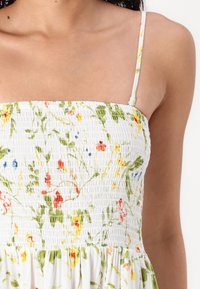 Λευκό φλοράλ φόρεμα με ραμμένο μπούστο, που διαθέτει πράσινα φύλλα και πολύχρωμα λουλούδια. Ρυθμιζόμενες λεπτές τιράντες και φαρδιά βάση.