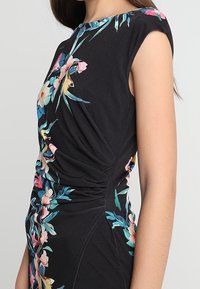 Schwarzes Kleid mit kurzen Ärmeln, das mit einem Blumenmuster in Pink und Blau gestaltet ist. Der Stoff ist an der Seite gerafft und schafft eine taillierte Silhouette.
