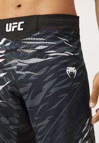 Black athletic shorts with a textured pattern of dark and light gray stripes. Features a black waistband with "UFC" logo and a white accent logo.