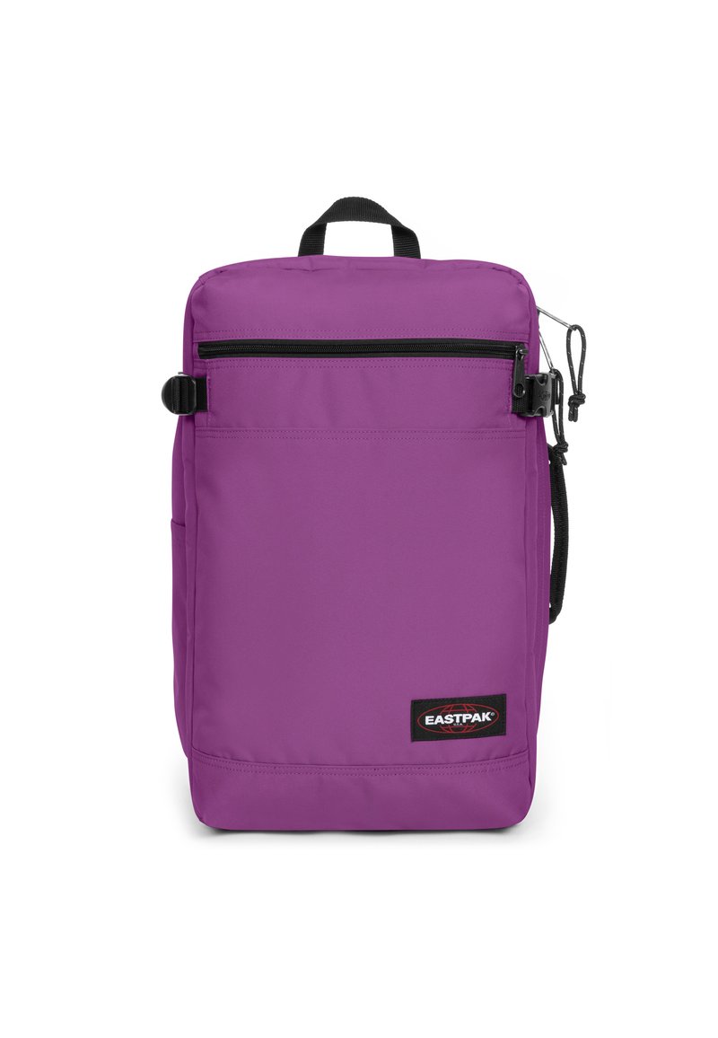 Mochila Eastpak morada con forma rectangular, que cuenta con un asa en la parte superior, un bolsillo frontal con cremallera y un parche con el logo en la parte inferior. Fabricada con tela duradera.