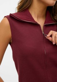 Bordeauxfärgad ärmlös topp med ribbad krage, hel dragkedja framtill och slät yta. Förstärkt med silverdetaljer vid dragkedjan.