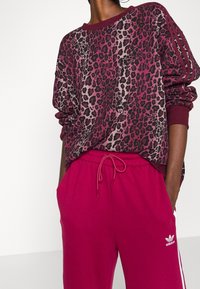 Leopardmönstrad sweatshirt med bourgogne-accenter, matchad med helrosa sweatpants med dragsko och sidostråkar, samt en Adidas-logotyp.