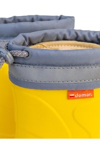 Żółta gumowa kalosza z szarym, teksturowanym mankietem z tkaniny. Posiada zamek ściągający oraz czerwoną metkę z nazwą marki "Demar."