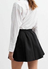 Gonna nera a pieghe con elastico in vita, abbinata a una camicia bianca a righe con polsini a bottoni e una vestibilità su misura.