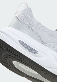 Närbild av vita och grå sneakers häldel som visar den stickade ovandelen, vadderad krage, dragflik och svart texturerad yttersula märkt "Cloudfoam Cushion".