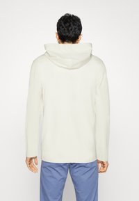 Hoodie med lång ärm i krämfärg, mjukt tyg, med en stor bakhuva och en enkel, strömlinjeformad skärning med sidofickor.