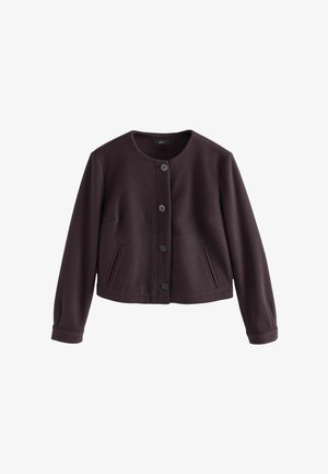 Kort lilla jakke lavet af glat stof, med rund halsudskæring, seks sorte knapper, og to frontlommer. Lange ærmer med tætsiddende manchetter.