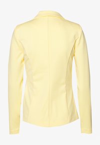 Žlutá bunda s dlouhým rukávem, která má přiléhavý střih, klopový límec a jemné detaily švů. Hladká textura a jednobarevný design. Lehce zakřivený lem.