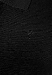 Polo noir en tissu tricoté texturé avec un petit logo brodé sur la poitrine. Design à col avec une coupe classique.