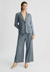 Světle modrý přiléhavý blazer s vyřezávanými klopami, jedním knoflíkem a dvěma kapsami. V kombinaci s kalhotami širokého střihu ze stejného materiálu, hladká textura.
