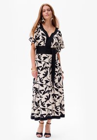 Maxi-jurk in crème met zwart loofpatroon, V-hals, korte mouwen, ceintuur in de taille, luchtige stof en zwarte accentrand.