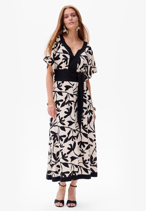 Robe maxi en crème avec motif de feuilles noires, décolleté en V, manches courtes, taille ceinturée, tissu fluide et accents de bord noir.