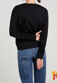Felpa nera con scollatura rotonda, polsini e orlo a costine, abbinata a jeans blu a vita alta. Design semplice e privo di decorazioni.