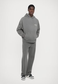 Gray hoodie with front pocket and logo, paired with matching gray sweatpants. Worn with black and white sneakers, smooth fabric texture.