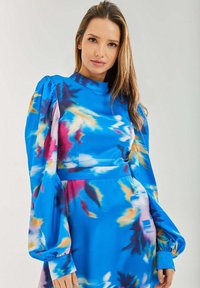 Long-sleeve dress in vibrant blue with abstract pink and yellow patterns, featuring a high neckline and gathered shoulder details.