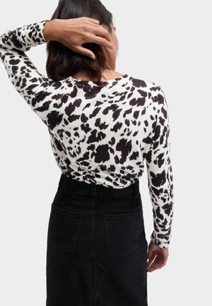 Maglione lavorato a maglia con stampa animale bianca e nera, maniche lunghe e scollo rotondo. Abbinato a una gonna di jeans nera a vita alta.