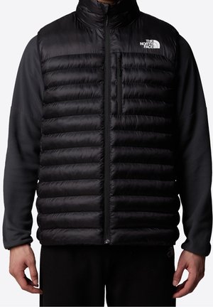 Veste matelassée noire avec manches en polaire, fermeture éclair à l'avant, poche poitrine et logo blanc The North Face sur le côté gauche de la poitrine.