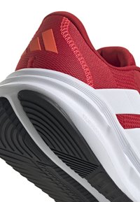 Sport shoes featuring a red mesh upper with textured accents, white midsole, and a patterned black rubber outsole for traction.