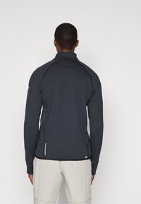 Pull en gris foncé à manches longues avec un col haut, en tissu texturé et avec des fentes sur les côtés, présentant un logo subtil et des détails cousus.