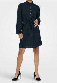Mörkblå skjortklänning med långa puffärmar, knapplängd framtill och knytmidja. Slätt tyg med en avslappnad passform, som slutar ovanför knäna.