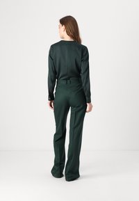 Green satin blouse with long sleeves and a round neckline, paired with high-waisted, wide-leg trousers, both featuring clean lines and a smooth finish.