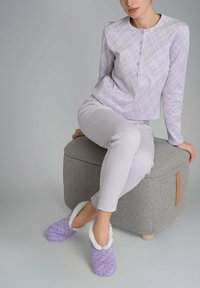 Maglietta a maniche lunghe di colore viola chiaro con un motivo a quadri, abbinata a pantaloni bianchi e ciabatte viola con una morbida fodera bianca.