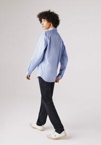 Camicia a quadri blu e bianca con maniche lunghe, abbinata a pantaloni navy e sneakers bianche. Progettata con una vestibilità rilassata e dettagli con bottoni.