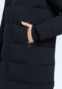 Schwarz gepolsterter Mantel mit einer seitlichen Reißverschlusstasche, strukturiertem Stoff und gerippten Bündchen, der Wärme und Funktionalität betont.