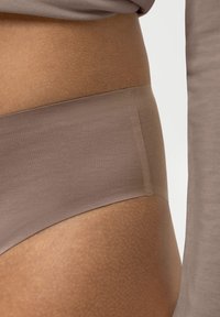 Braghette in cotone beige con una texture liscia, caratterizzata da una vita alta e un design senza cuciture, insieme a un top aderente a maniche lunghe dello stesso colore.