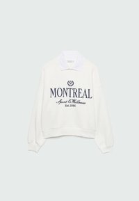Sweat-shirt blanc à manches longues avec col blanc, texte bleu marine "MONTREAL Sport & Wellness Est. 1986" et un petit emblème de raquette de tennis sur la poitrine.