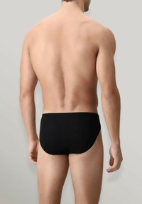 Slip da nuoto neri con una texture liscia, design a vita bassa e copertura minima. Il tessuto sembra elastico e mantiene una silhouette aderente.