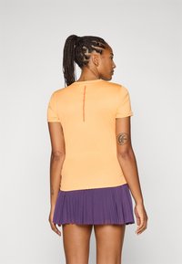 En person med fletter har på seg en oransje sportsbekledning og et plissert lilla skjørt, sett fra ryggen, som viser frem stilen deres og tatoveringene.