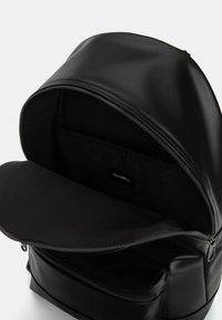 Czarny skórzany plecak z rozpiętą główną komorą, w której widać wewnętrzną kieszeń z oznaczeniem "PULL&BEAR" oraz zamkniętą przednią kieszenią na zamek.