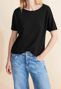 Černé tričko s krátkým rukávem v uvolněném střihu, vyrobené z lehké tkaniny. Kombinováno se světle modrými džíny s jemně vyšisovanou texturou.