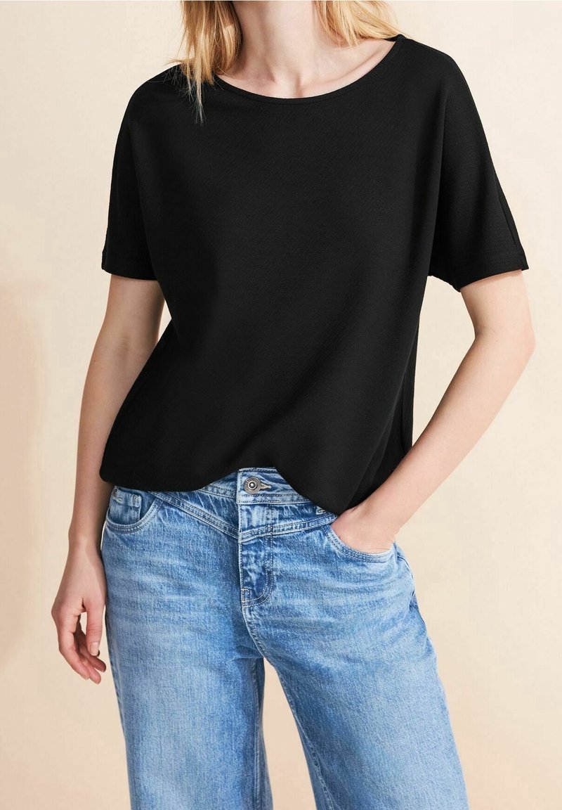 Černé tričko s krátkým rukávem v uvolněném střihu, vyrobené z lehké tkaniny. Kombinováno se světle modrými džíny s jemně vyšisovanou texturou.