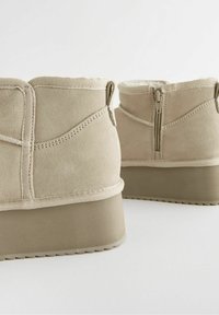 Beżowe botki za kostkę wykonane z miękkiego materiału przypominającego zamsz, z zapięciem na zamek, wyściełanym kołnierzem oraz grubą podeszwą platformową z teksturą w rowki.