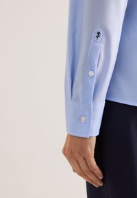 Lichtblauw overhemd met lange mouwen, voorzien van een gladde textuur, een puntige manchetknoop met twee knopen en een geborduurd bloemmotief op de manchetknoop.