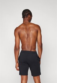 Mustat urheilushortsit, joissa on sivutaskut ja pehmeä, joustava kangas. Takakuvassa näkyy muotoiltu istuvuus vyötärön ja säärten ympärillä.