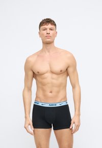 Czarne obcisłe bokserki z jasnoniebieskim pasem z logo Nike, noszone przez modela bez koszulki na neutralnym tle.