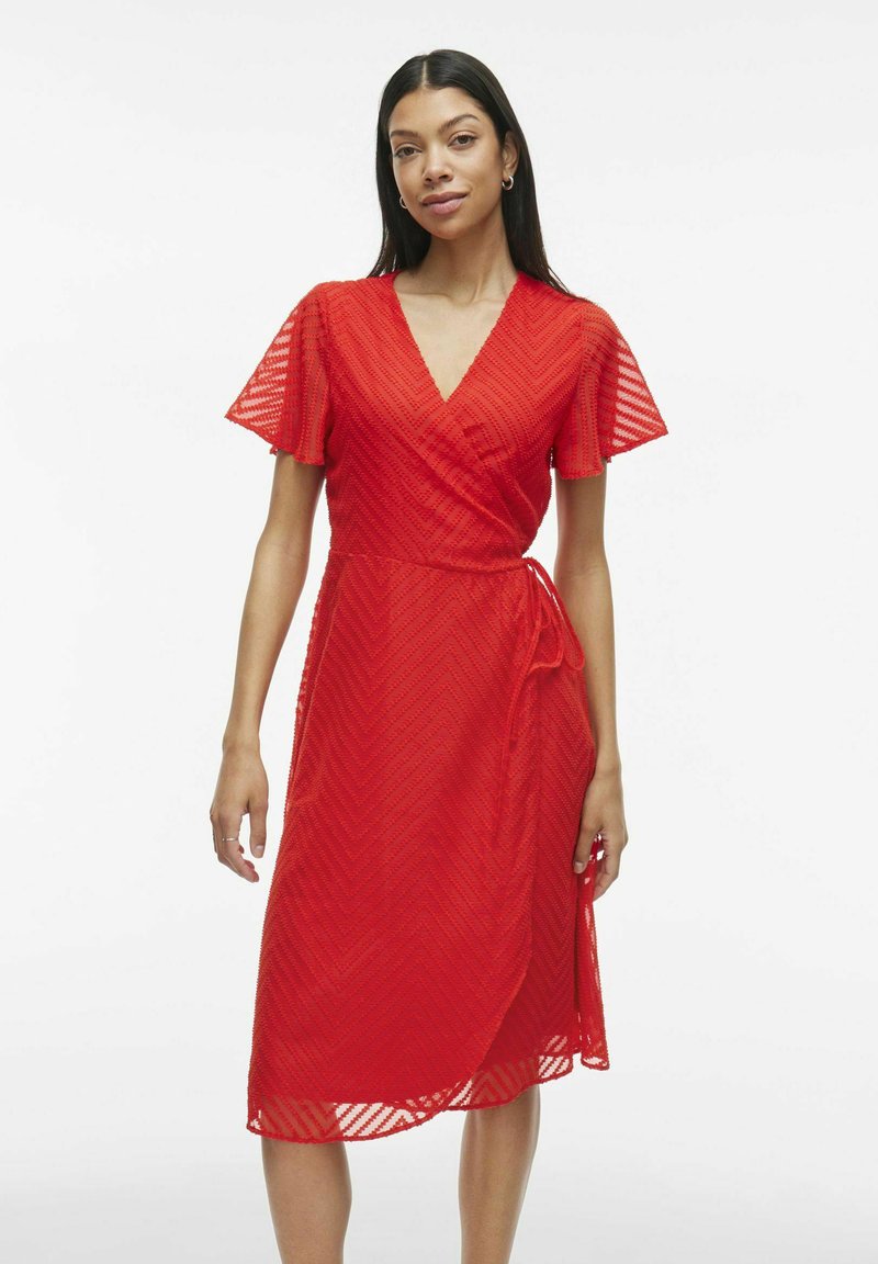 Rochie înfășurată roșie, texturată, cu mâneci scurte, decolteu în formă de V și curea în talie. Prezintă un model în zig-zag pe întreaga țesătură.
