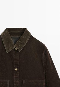 Donkerbruine corduroyjas met knoopsluiting, grote kraag en voorkruiken, weergegeven op een witte achtergrond.