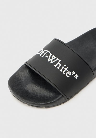 Μαύρο σανδάλι με φαρδιά λωρίδα που φέρει λευκή επιγραφή "Off-White™". Η υφή είναι λεία με πατημένο πέλμα για καλύτερο κράτημα.