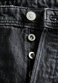 Zwarte denim jeans met een gladde textuur, metalen knoopsluiting en metalen drukknoopsluitingen, met zichtbare stiksels.