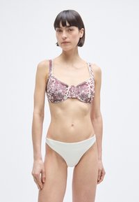 Σετ μπικίνι με μπορντό τοπ με μπανέλα και κρεμ λεπτομέρειες, φαρδιές τιράντες, συνδυασμένο με λευκό σλιπ χαμηλής μέσης.