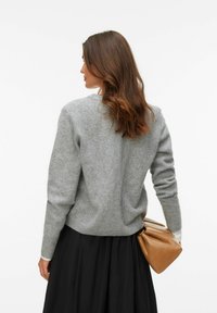 Grå stickad tröja med rund halsringning och långa ärmar. Kombinerad med en flödande svart kjol och en beige väska, vilket skapar ett lager-på-lager-uttryck.