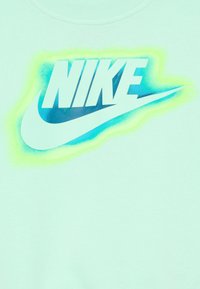 Svetlo mentolový svetre s veľkým bielym logom Nike obrysom v modro-zelenom graadiente, s hladkou textúrou a dizajnom s okrúhlym výstrihom.