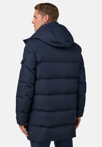 Námorně modrá péřová bunda s kapucí, která má vodorovné prošívané panely, boční kapsy a logo na dolním lemu. Hladká, strukturovaná látka.