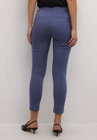 Fitted, ankle-length trousers made from a soft, light blue fabric with a smooth texture. Features faux pockets and a rolled hem. Paired with black heels.
