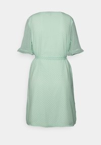 Vestido verde menta com mangas curtas, padrão de bolinhas, cintura ajustada e tecido fluido. A parte de trás apresenta um design de decote simples.