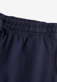 Navy plave jogger hlače s elastičnim pojasom i vezicom, izrađene od mekog pamuka, s glatkom, mat teksturom.